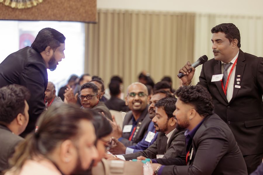 A member speaking on the microphone while the tables around him laugh
