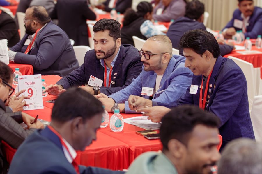 Three members in discussion at Table 9 with a busy hall behind them